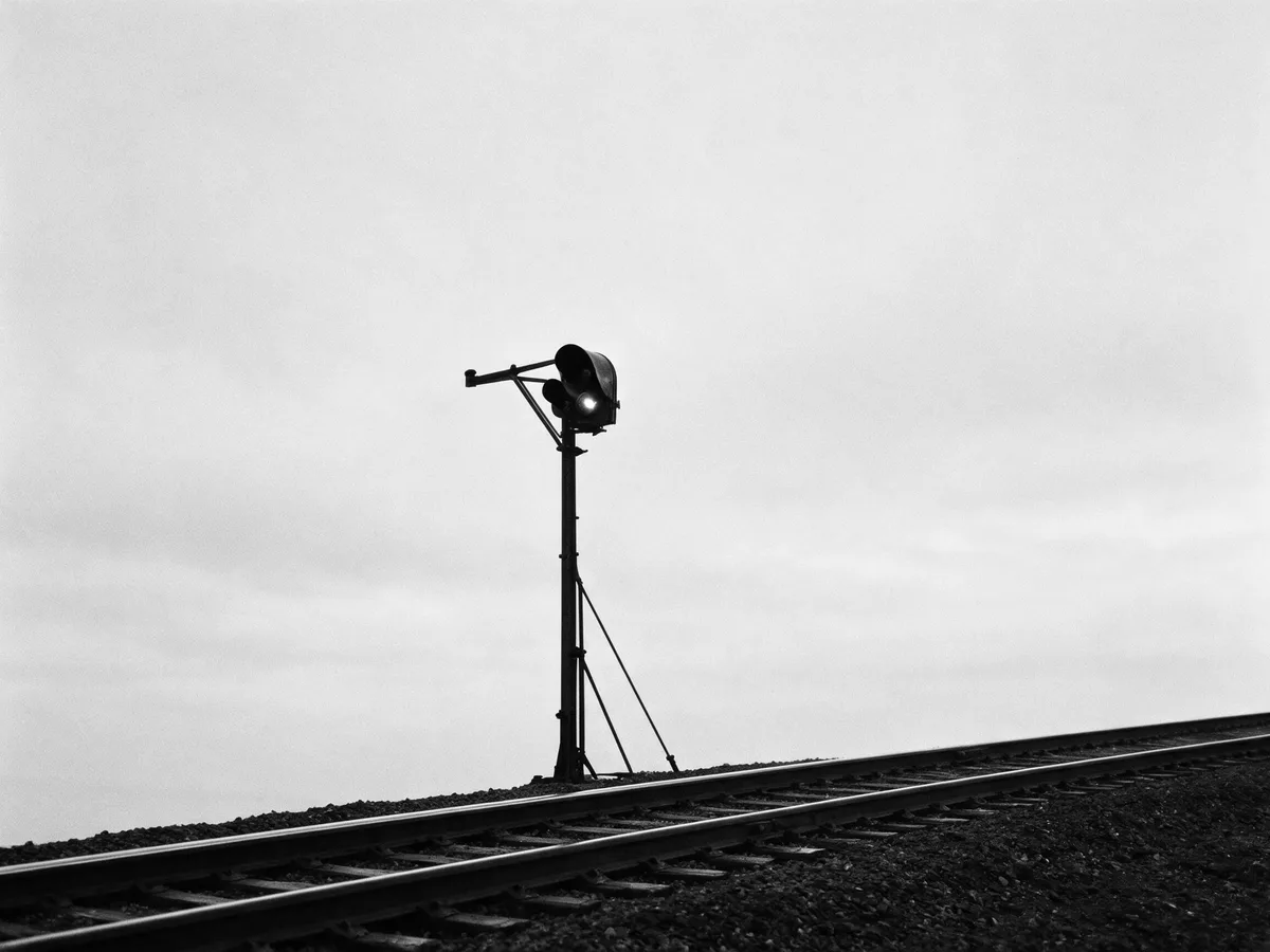 A single railway signal standing against an empty sky above a track, in black and white.