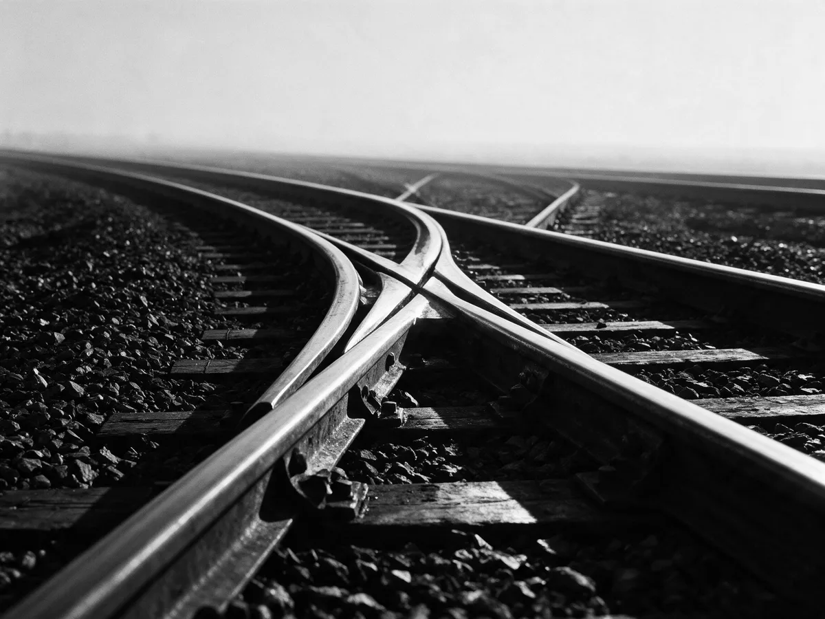 Two sets of rails crossing at a switch and running out to the horizon, in black and white.